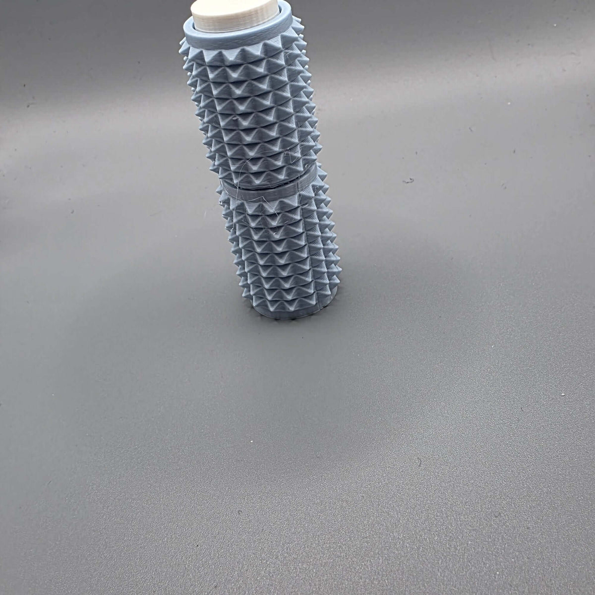 A light blue textured cylindrical bottle with a ridged, spiky exterior and a white cap, standing upright on a smooth gray surface.