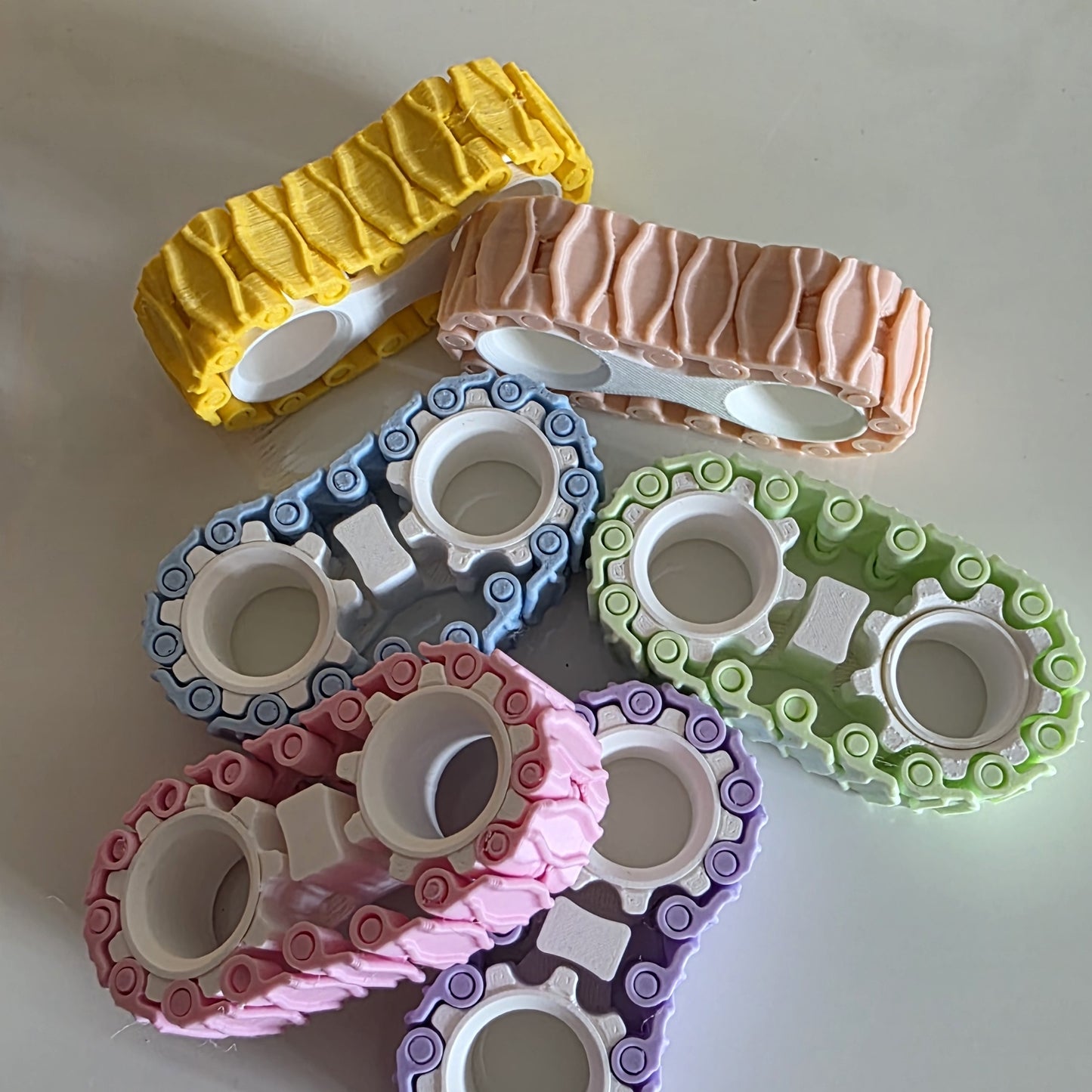 Six colorful, flexible plastic rings with a wavy, treaded outer surface and white circular centers, arranged on a plain light background in yellow, peach, blue, green, pink, and purple.