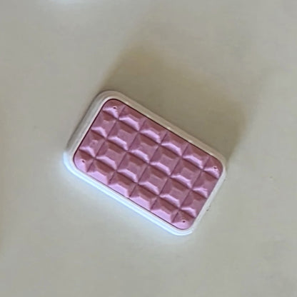 A pink rectangular textured item with a white border, photographed on a plain light beige background.