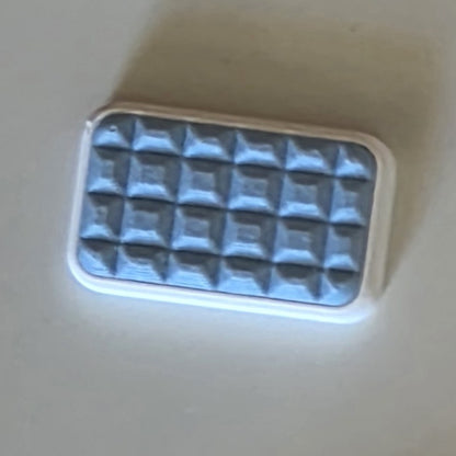 A small rectangular cosmetic item with a white border and a textured, quilted sky blue, photographed on a plain light beige surface.
