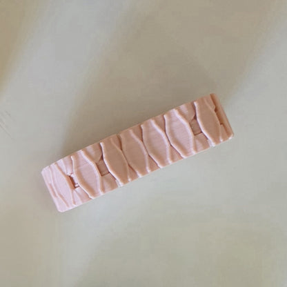 A light pink textured hair claw clip with a raised, segmented scale-like pattern, shown on a neutral cream-colored background.