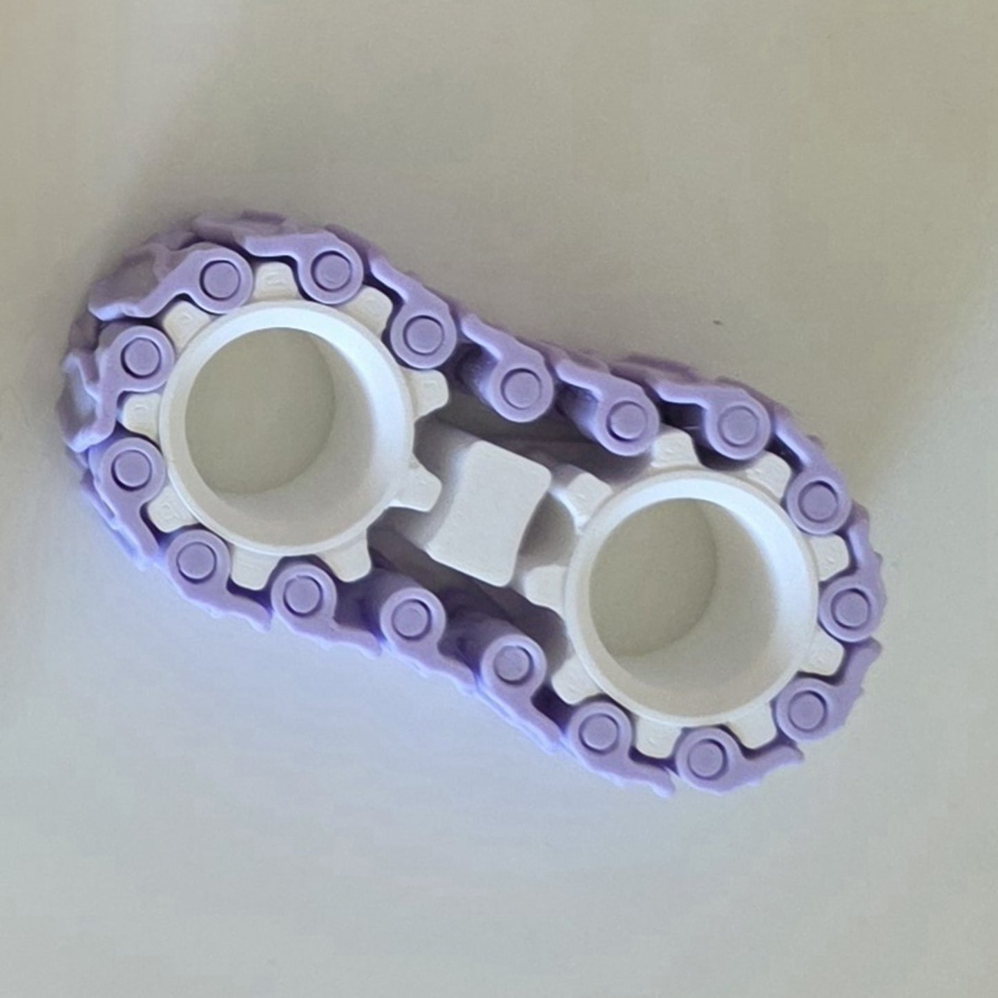 A purple and white plastic toy component with two circular openings and a chain-like outer structure, photographed on a plain light background.