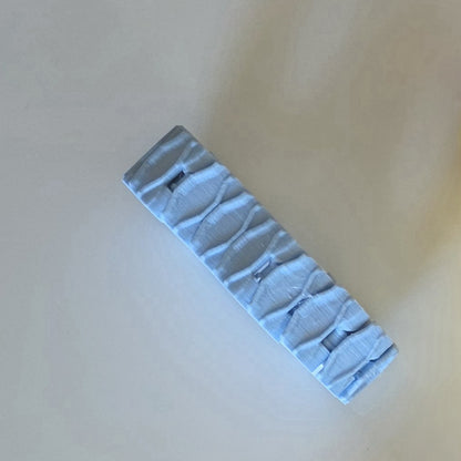 A light blue textured hair claw clip shown diagonally on a plain beige background.