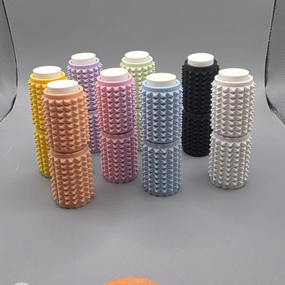A set of eight textured cylindrical containers with white screw-on caps, arranged in two rows on a gray background. The containers come in multiple colors, including yellow, peach, pink, lavender, mint green, light blue, black, and white, each featuring a raised diamond pattern on their sides.
