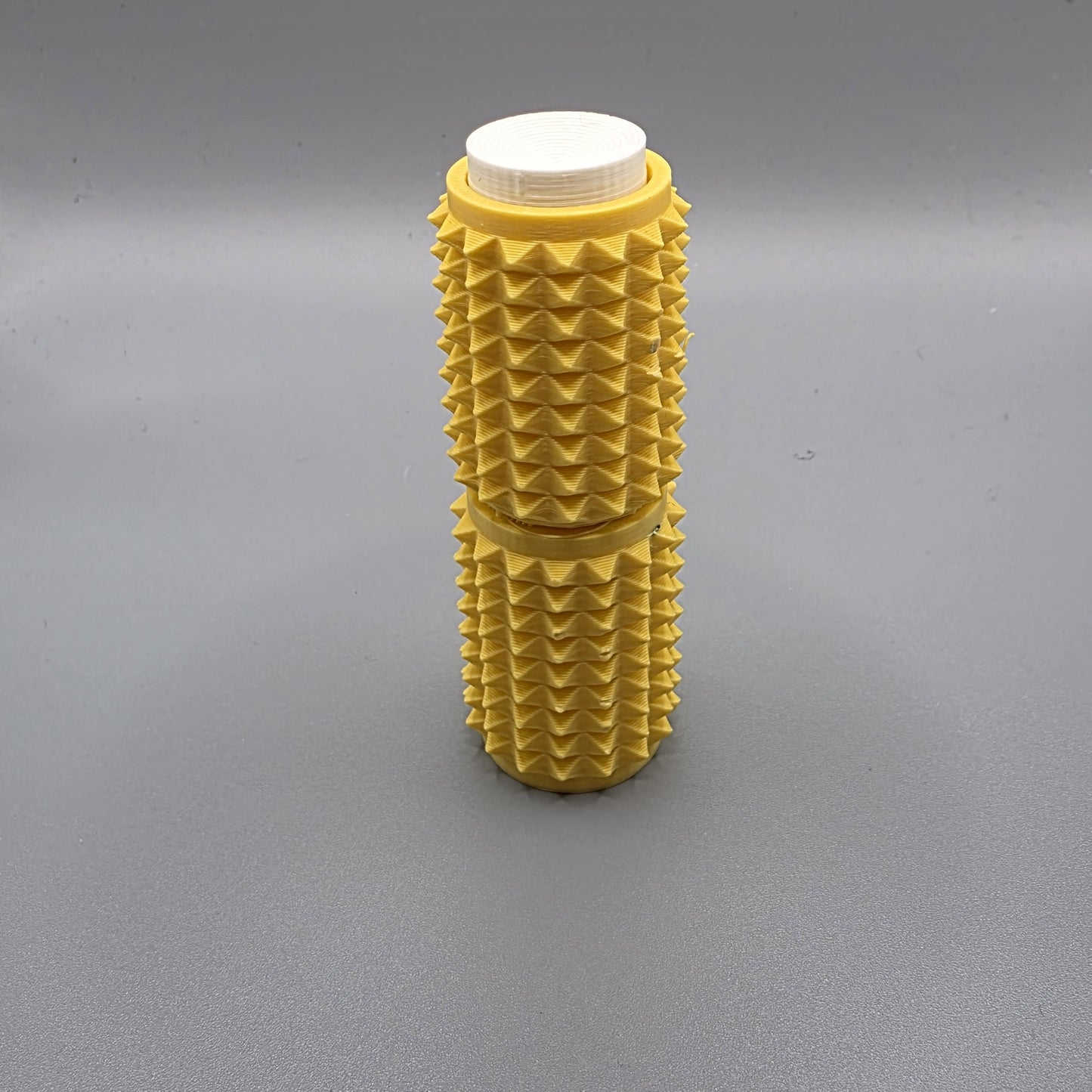 A yellow textured foam roller with a white cap, standing upright on a gray surface.