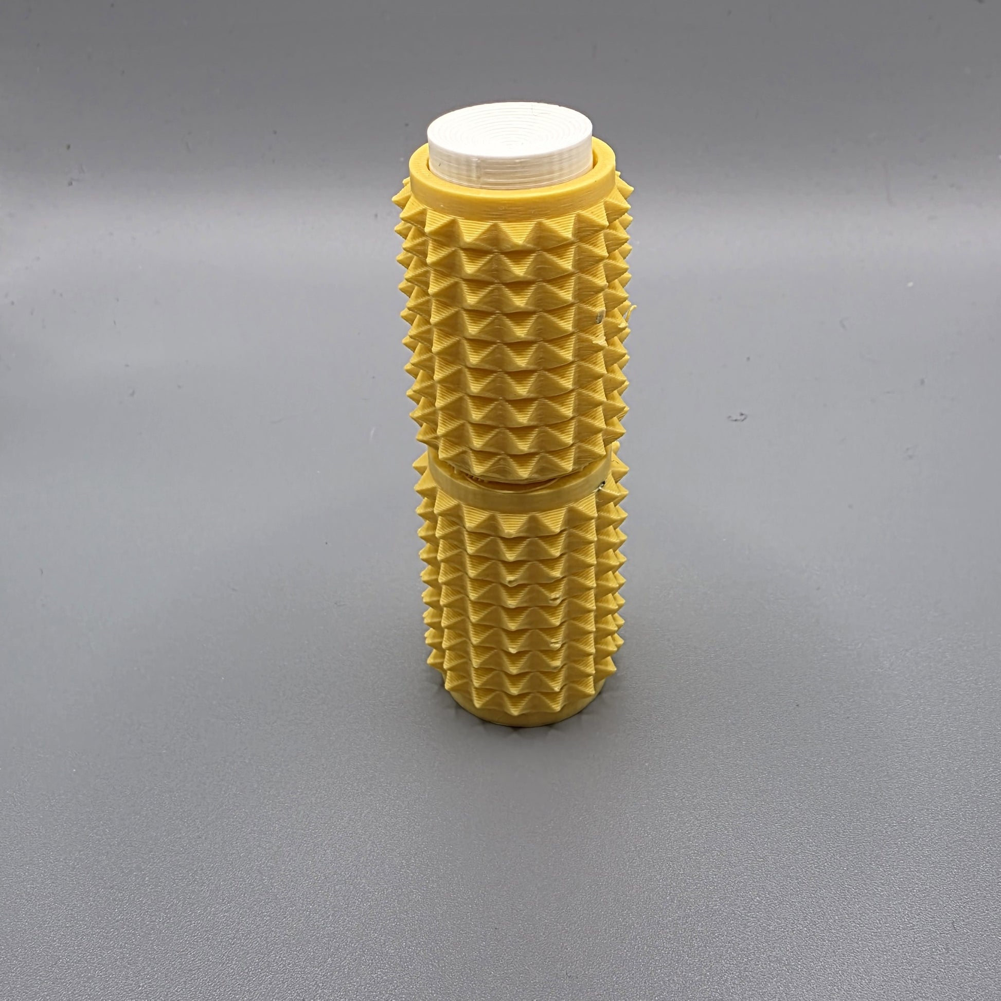 A yellow textured foam roller with a white cap, standing upright on a gray surface.