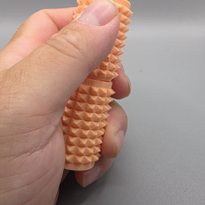 A close-up of a hand holding a textured, peach-colored silicone or rubber object with a ridged, spiky surface against a plain gray background.