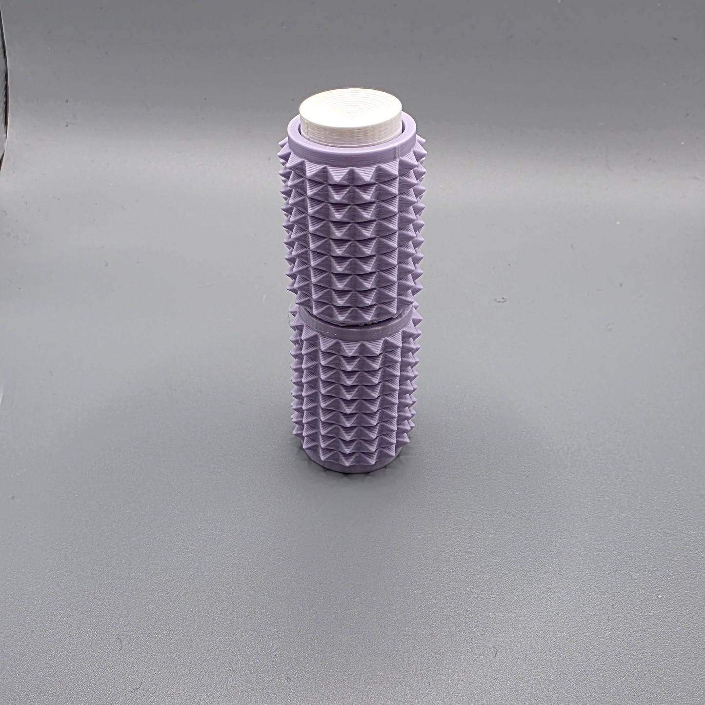 A lavender purple textured cylindrical container with a white screw-on cap, standing upright on a neutral gray background.