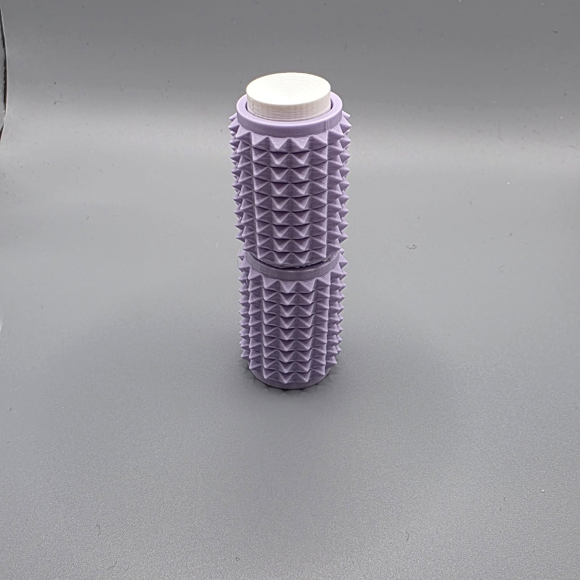A lavender purple textured cylindrical container with a white screw-on cap, standing upright on a neutral gray background.