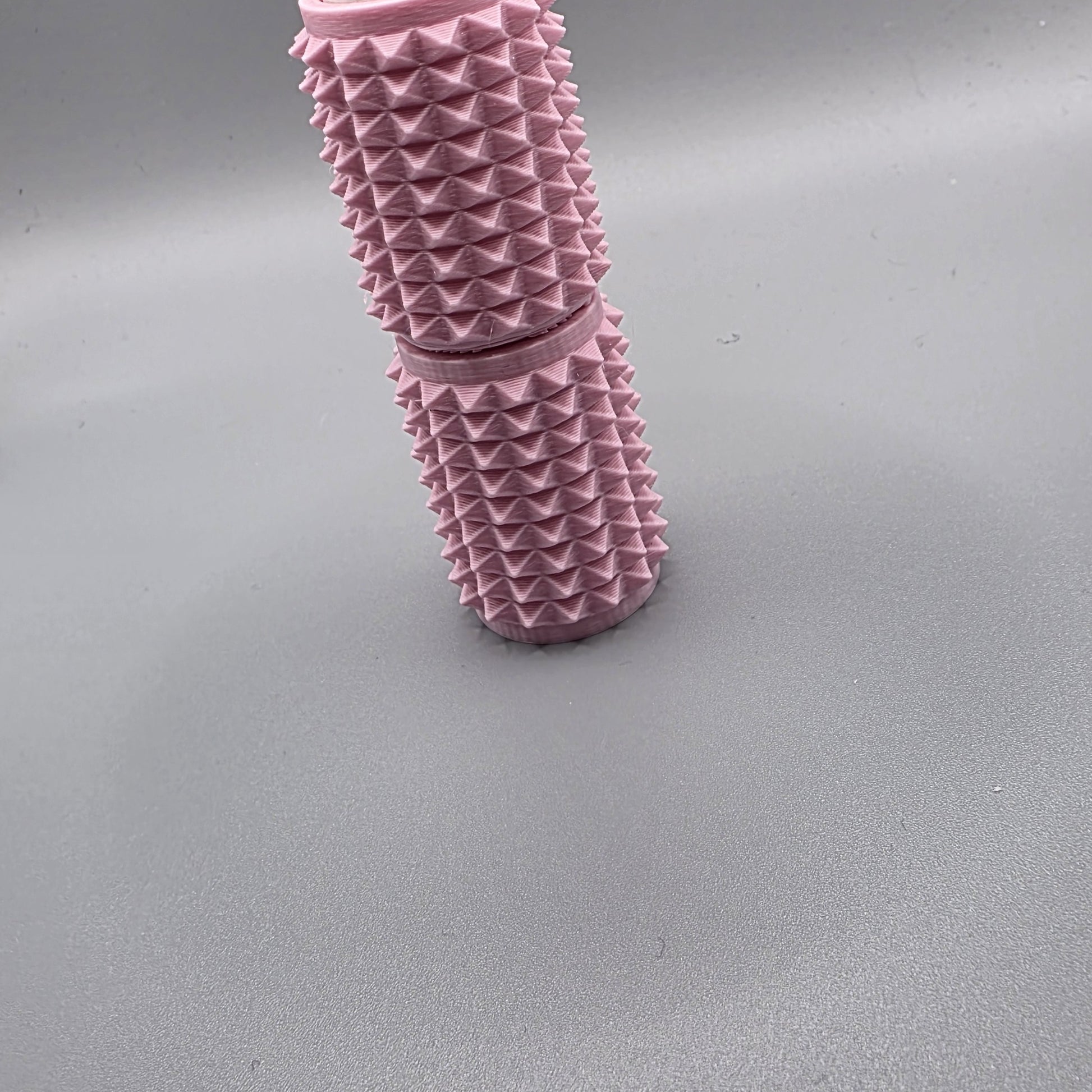 A pink textured cylindrical product with a raised pyramid pattern, standing upright on a smooth gray surface.