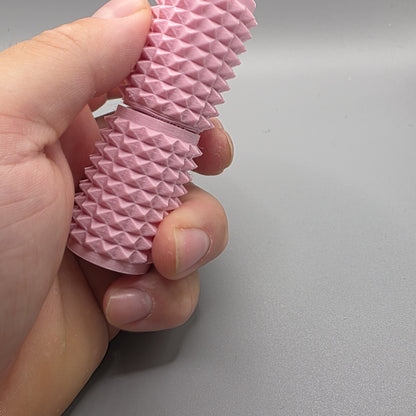 A close-up of a hand holding a pink textured silicone sleeve with a ridged, pyramid-patterned surface against a plain gray background.