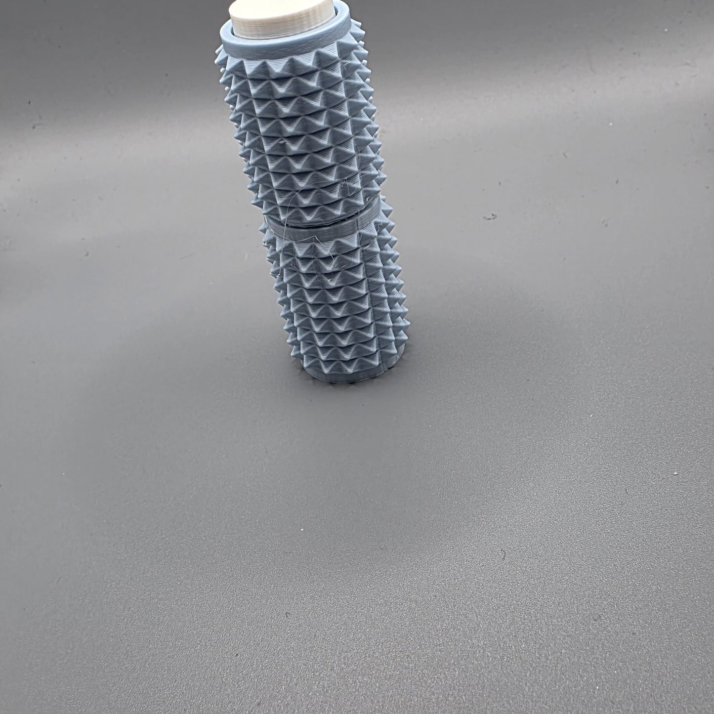 A light blue textured cylindrical bottle with a ridged, spiky exterior and a white cap, standing upright on a smooth gray surface.