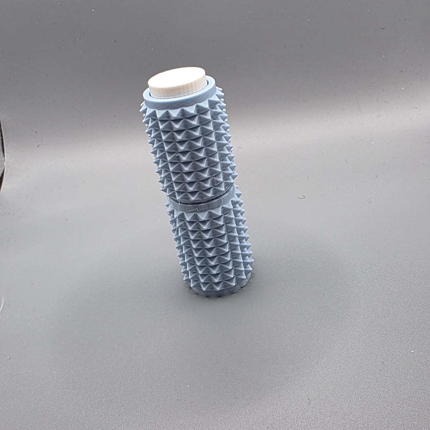 A light blue textured cylindrical container with a white screw cap, standing upright on a gray background.