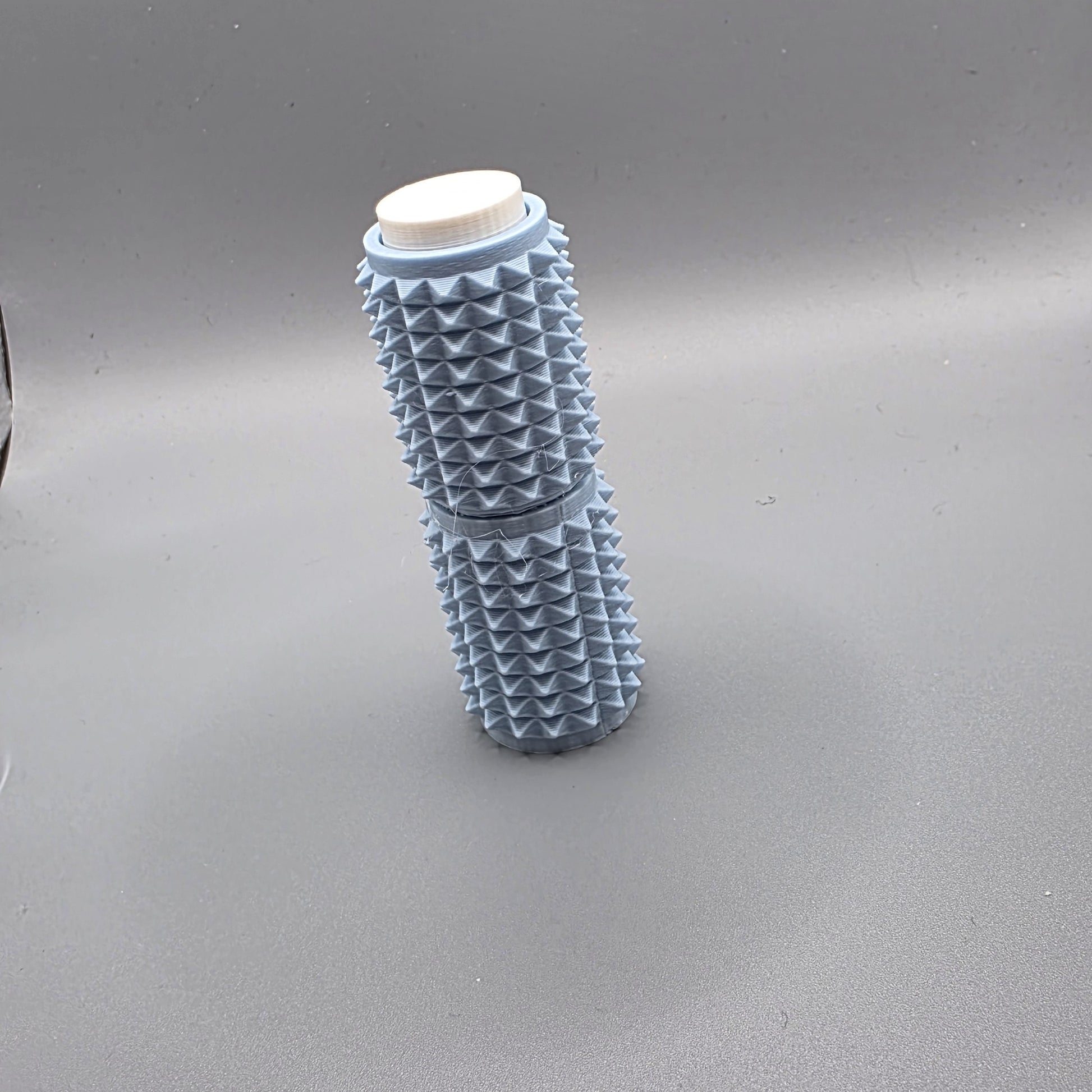 A light blue textured cylindrical container with a white screw cap, standing upright on a gray background.