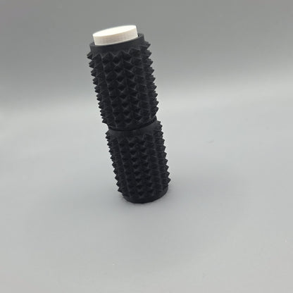 A black textured cylindrical object with a white circular top, standing upright on a smooth gray surface.