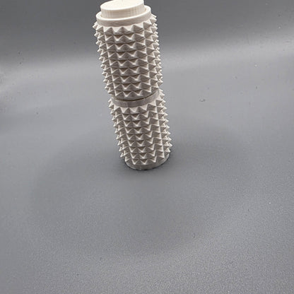 A white textured cylindrical container with a ribbed, spiky surface and a screw-on cap, standing upright on a gray surface.