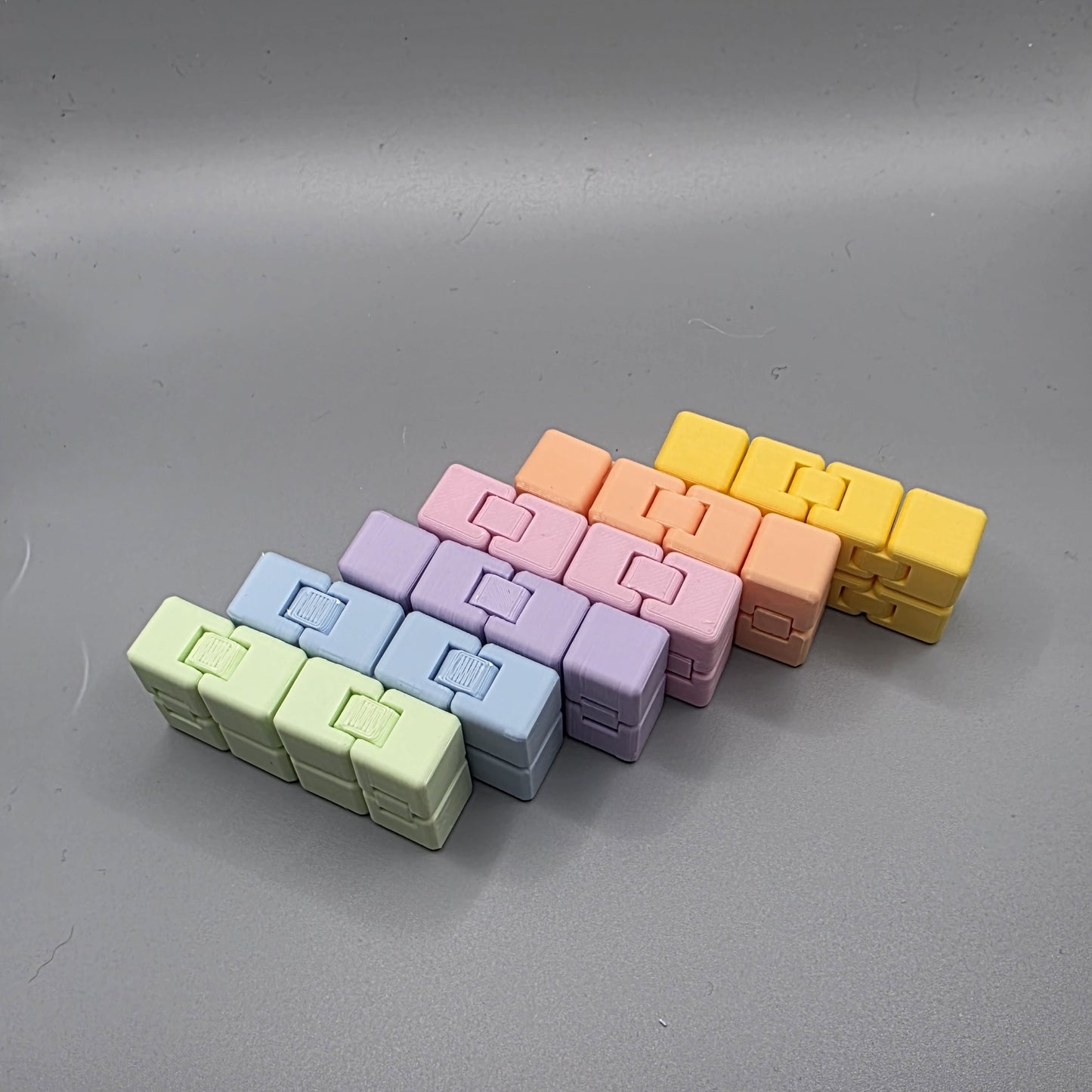 Six small rectangular plastic pieces in pastel colors arranged in two staggered rows on a smooth gray surface. The colors visible are light green, light blue, lavender, pink, peach, and yellow.