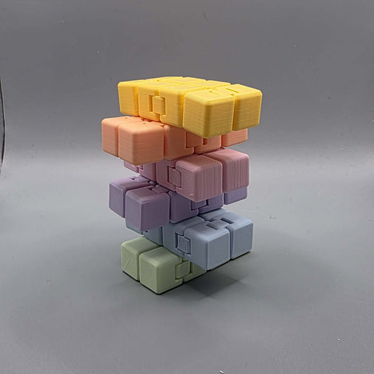 A stack of modular 3D-printed cube blocks in pastel colors, including yellow, peach, pink, lavender, light blue, and sage green, arranged on a neutral gray background.