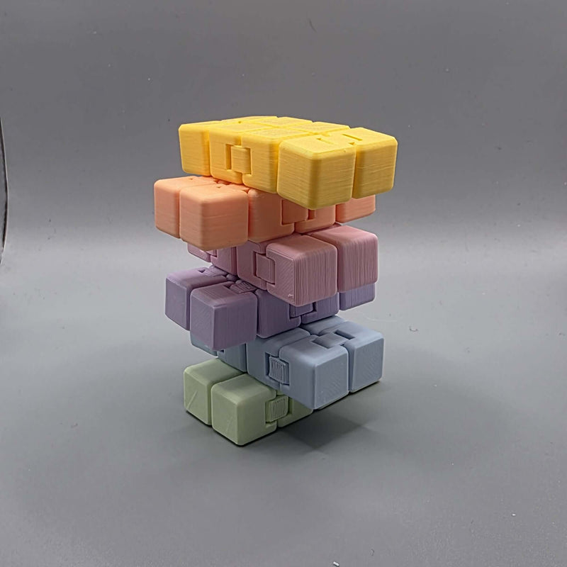 A stack of modular 3D-printed cube blocks in pastel colors, including yellow, peach, pink, lavender, light blue, and sage green, arranged on a neutral gray background.