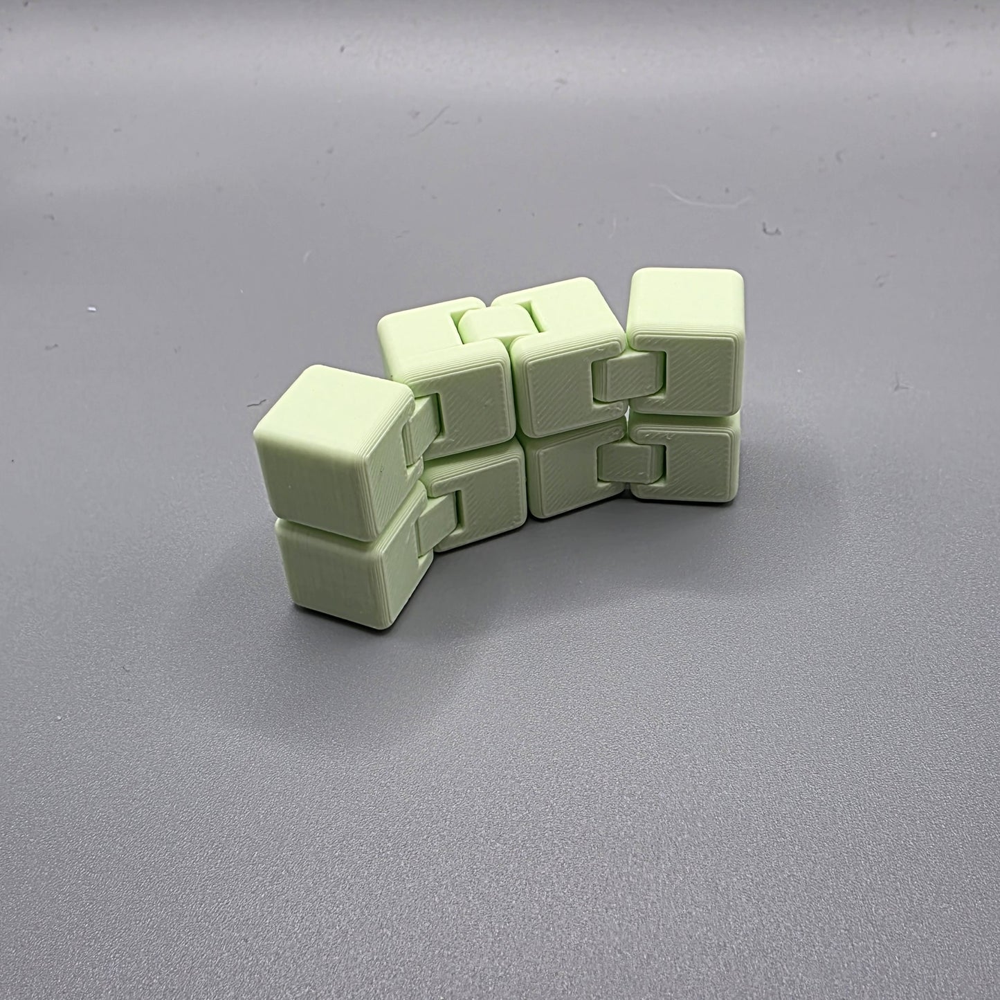 A light mint green plastic fidget cube toy with interlocking cube segments, displayed on a neutral gray background.