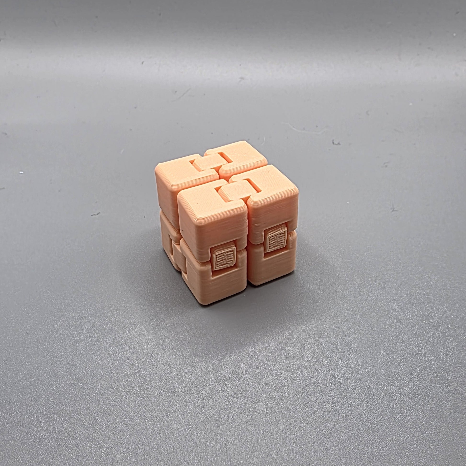 A small peach-colored plastic puzzle cube with four interlocking cube-like sections, photographed on a smooth gray surface.