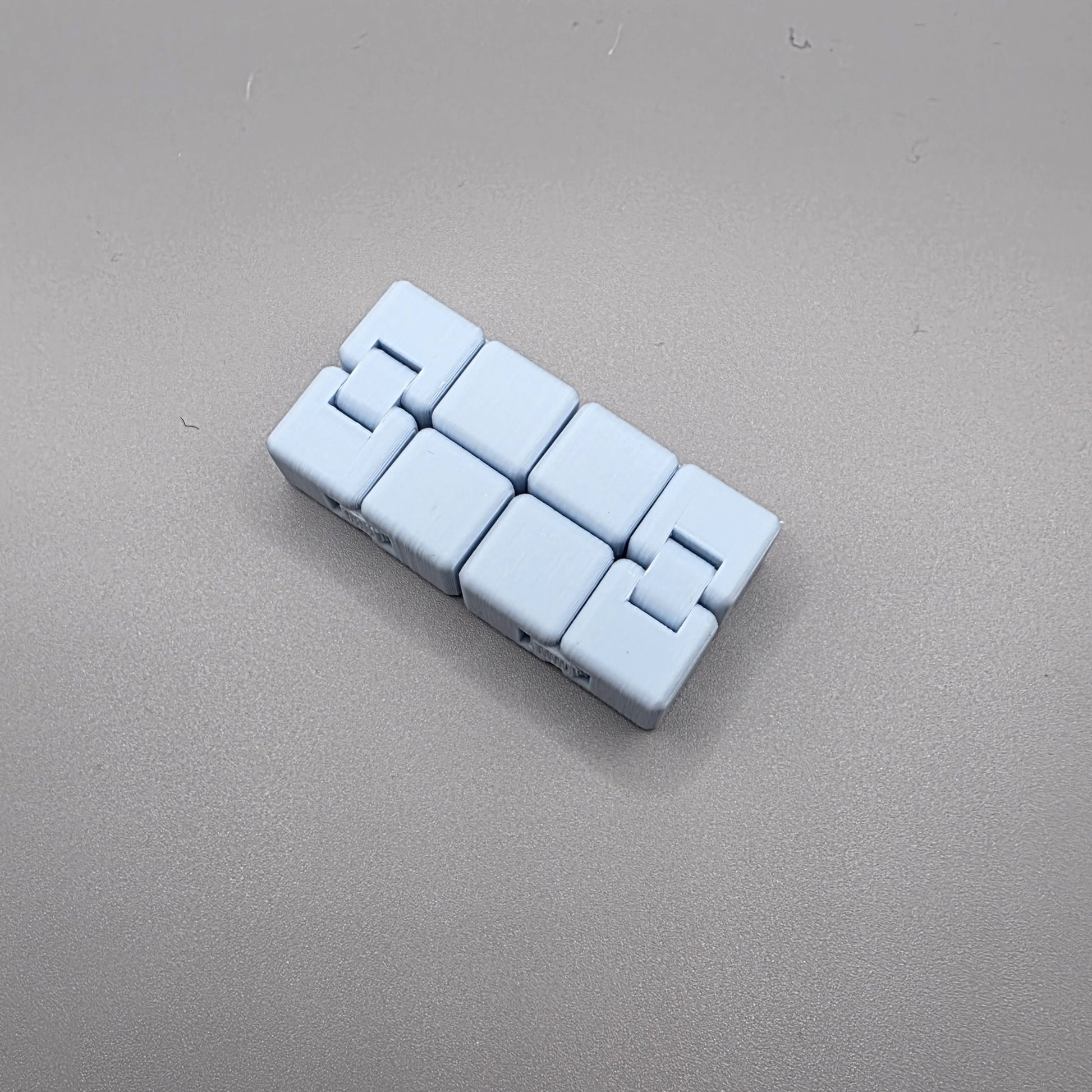 A light blue plastic interlocking cube puzzle piece set, arranged in a row on a neutral gray textured background.