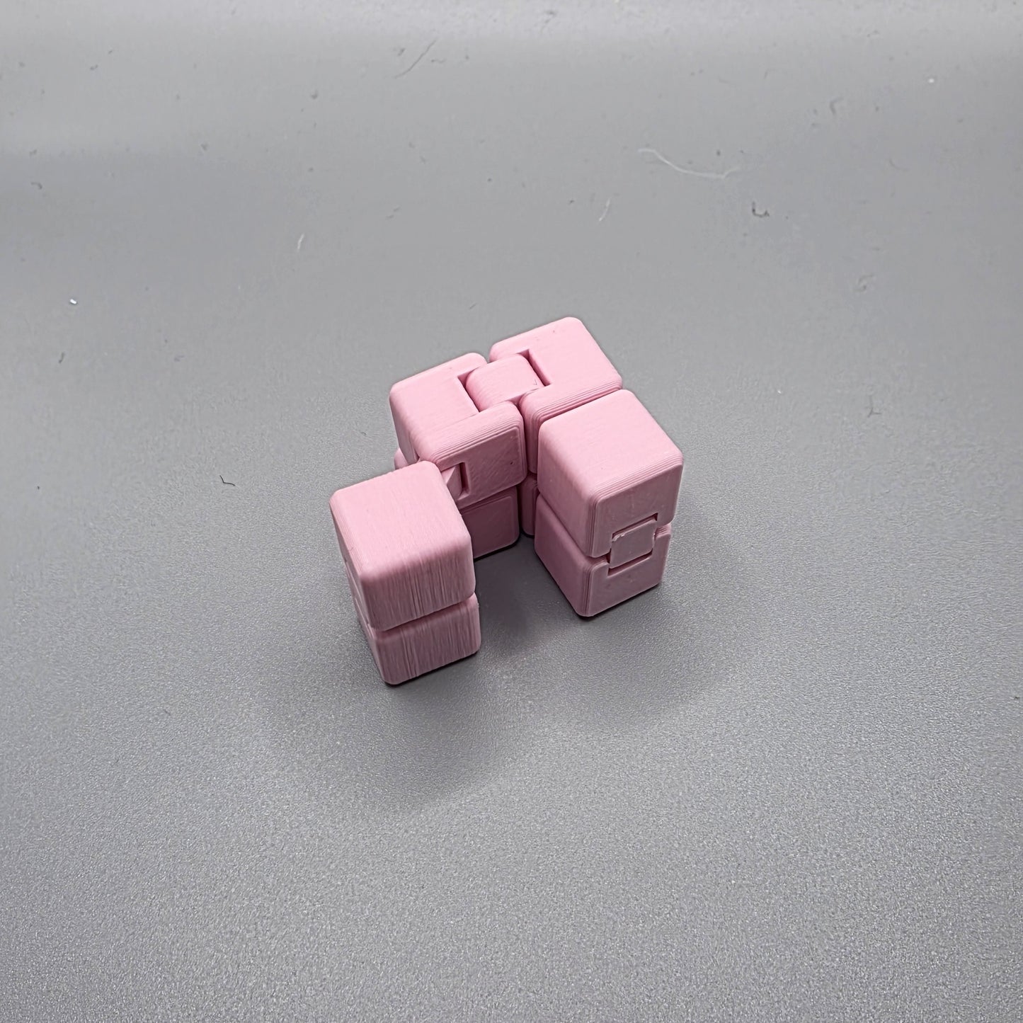 A pink plastic cube puzzle toy with interlocking cube sections, photographed on a plain gray surface.