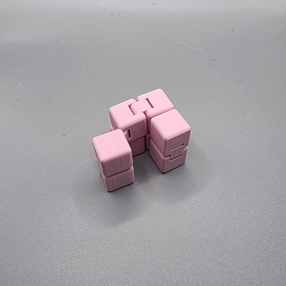 A pink plastic cube puzzle toy with interlocking cube sections, photographed on a plain gray surface.