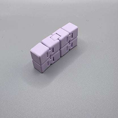A small lavender-colored 3D-printed puzzle toy made of interlocking cube-like pieces, photographed on a smooth gray surface.
